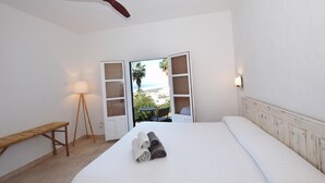 A bedroom with a bed, a ceiling fan, a bench, and a view through an open door.