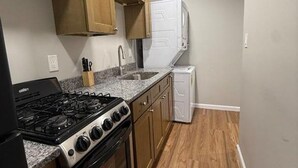 A compact kitchen with wooden cabinets, a gas stove, a built-in oven, a sink, and a white refrigerator.