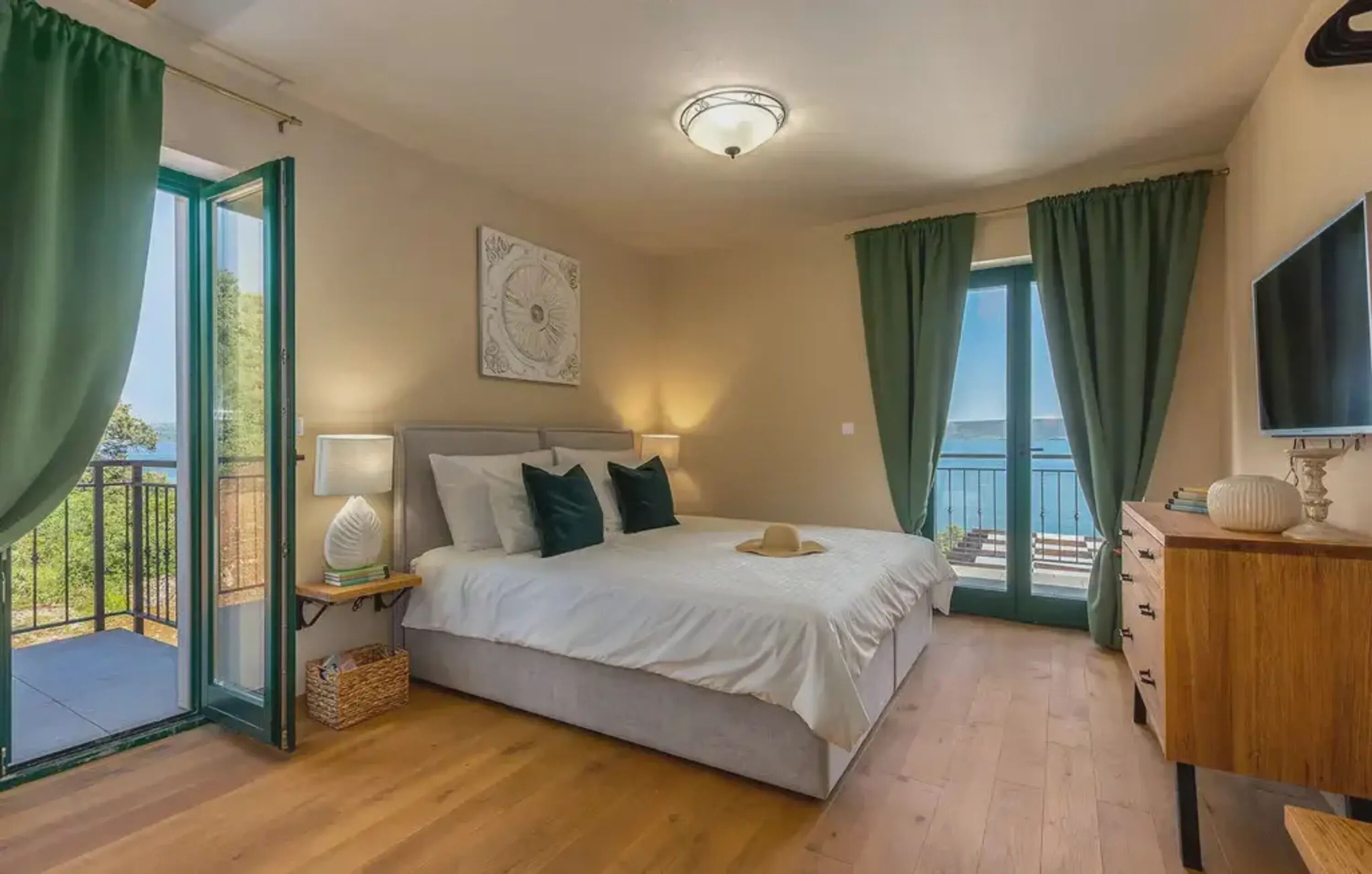 A bedroom with a bed, a nightstand, a dresser, a TV, and a balcony with curtains.