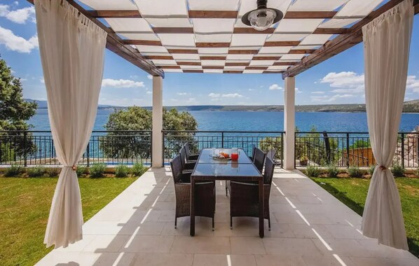 A covered outdoor dining area with a table and chairs, overlooking a body of water. - Villa Sadic Nearby Zadar - Crovillas (Posedarje)