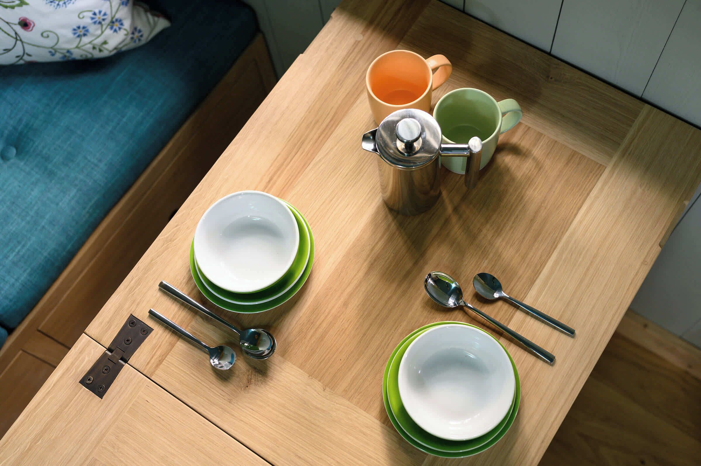A wooden table with stacked plates, a teapot, and two mugs.