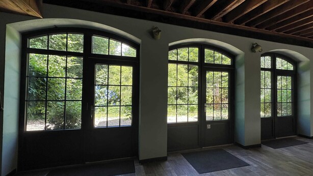 A room with large arched windows, a wooden ceiling, and a dark floor.