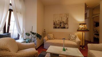 A cozy living room with a sofa, two armchairs, a coffee table, and a cityscape painting on the wall.