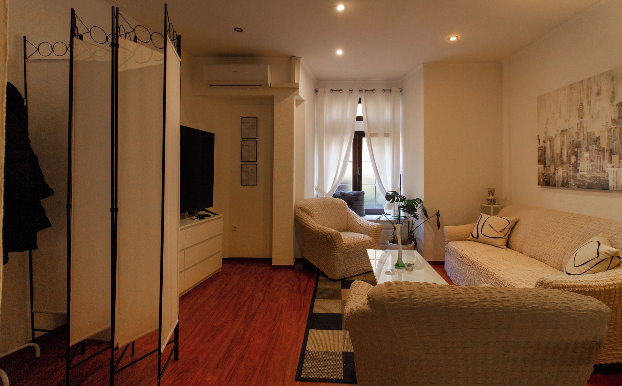 A modern living room with a sofa, armchair, and a television on a stand.