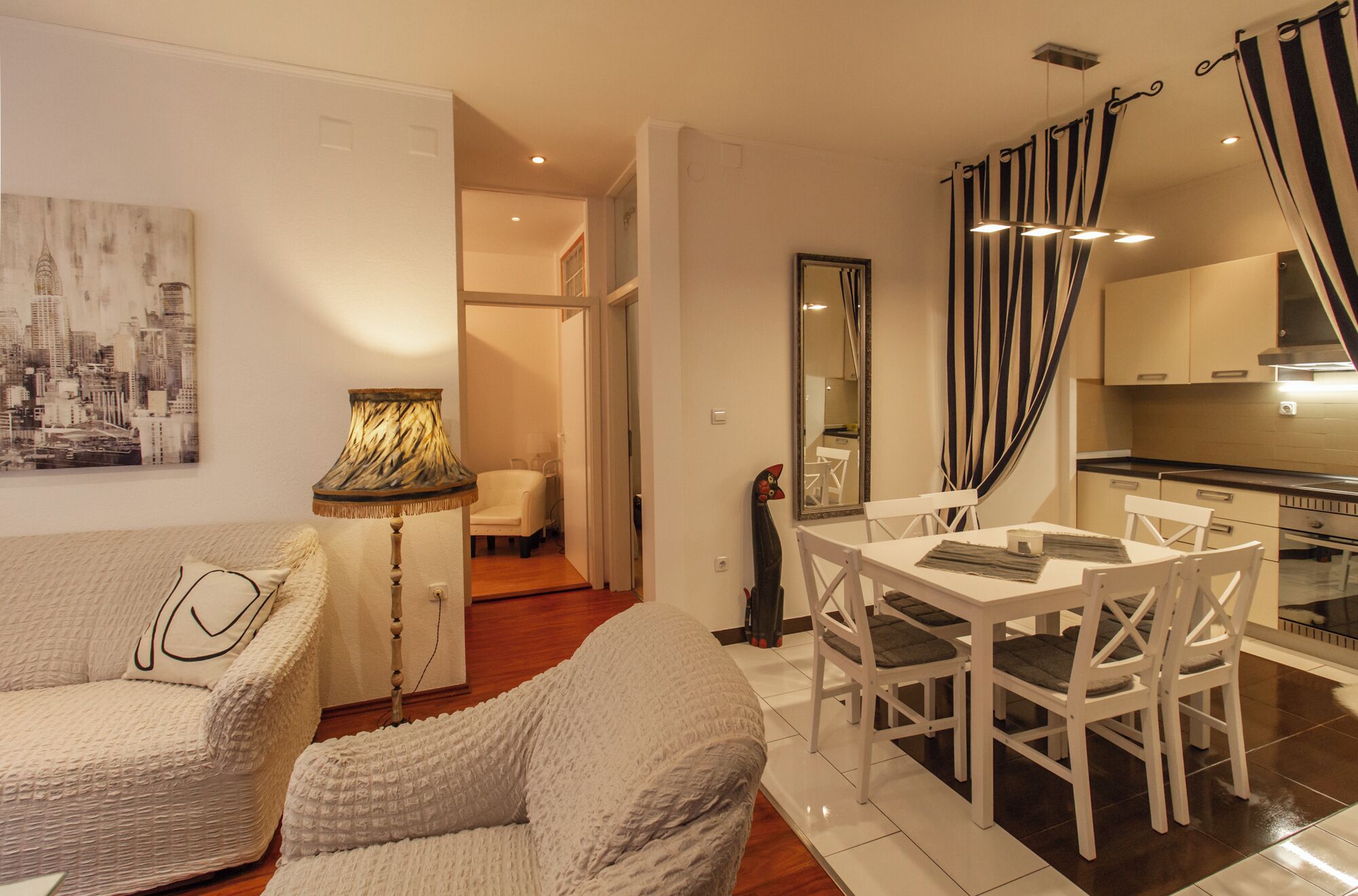 A cozy living room with a sofa and a dining table with chairs. There is a kitchen area with a stove and cabinets.