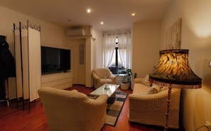 Een woonkamer met een televisie, een bank, een fauteuil, een salontafel en een lamp.