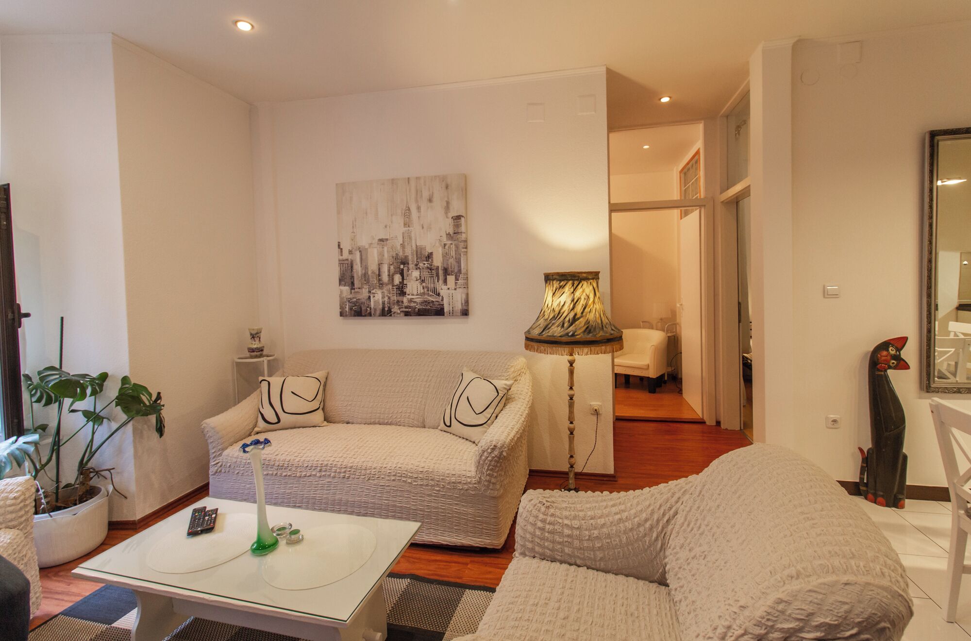 A living room with a sofa, a coffee table, and a lamp. There is a painting on the wall and a mirror on the right.