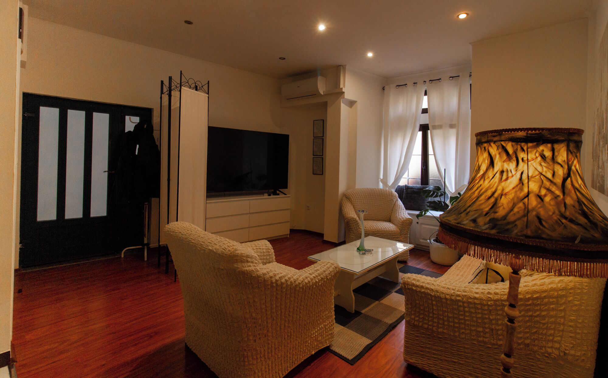 A living room with a flat-screen TV, two beige armchairs, a coffee table, and a decorative lamp.