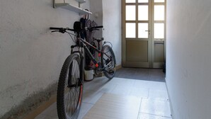 Un corridoio stretto con una bicicletta appoggiata al muro, una porta con pannelli di vetro e un pavimento in piastrelle bianche.