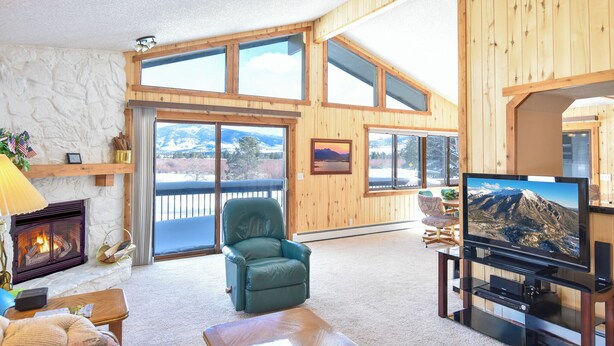 Ein geräumiges Wohnzimmer mit Kamin, Fernseher und großem Fenster mit Blick auf eine verschneite Landschaft.