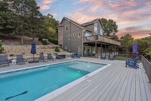 A pool area with a wooden deck, lounge chairs, and a building with a balcony. - Van Kirk Cove 6 BDR Stunner! (Branson West)