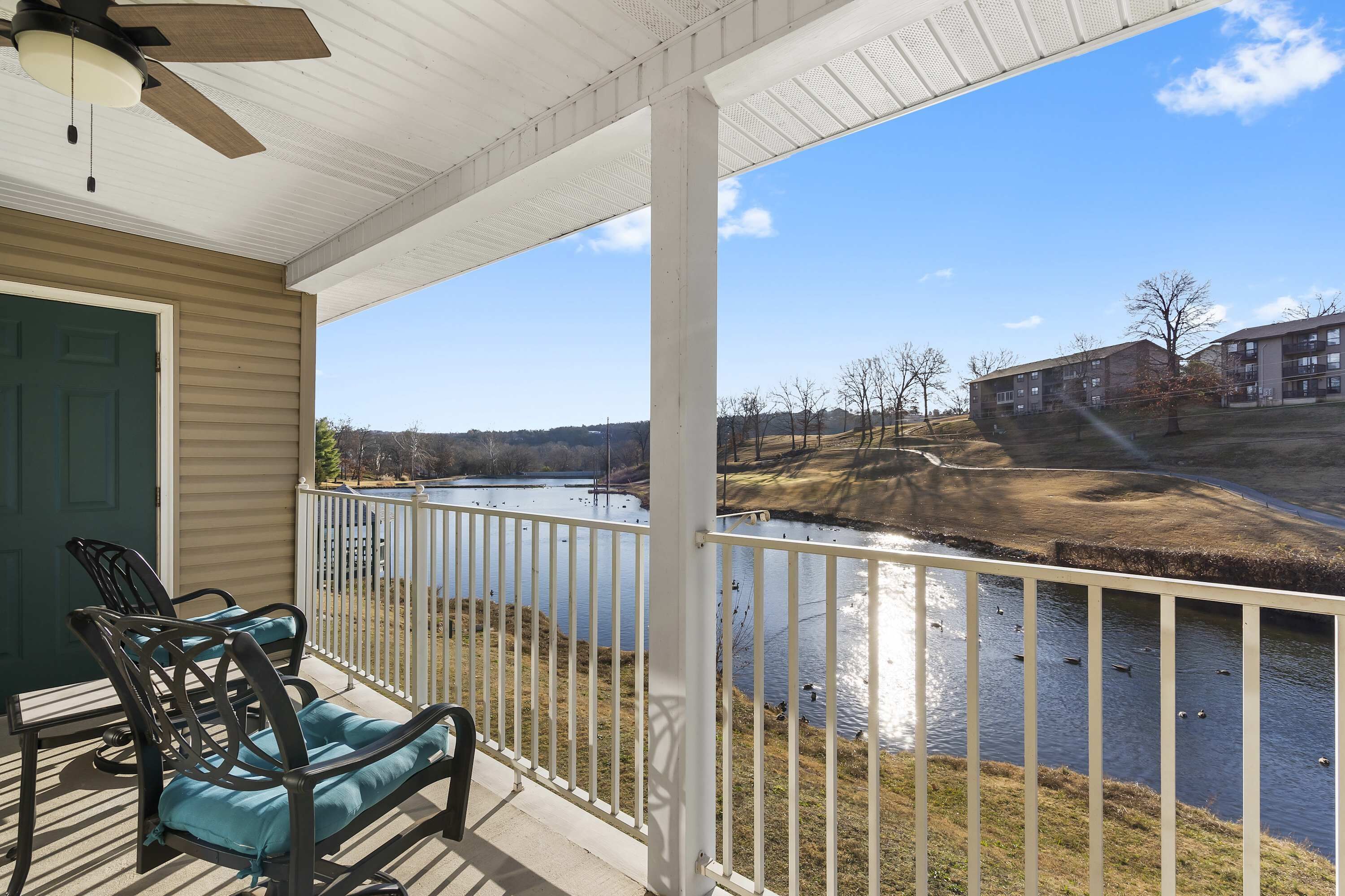 A covered porch with a view of a lake and buildings in the background.