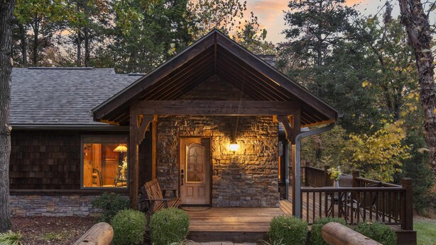 A rustic cabin with a stone exterior, a wooden porch, and a well-lit entrance. - The Cabin at Rock Canyon (Branson)
