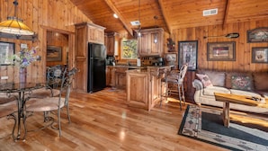 A spacious kitchen with wooden cabinets, a black refrigerator, and a dining area with metal chairs and a table. - The Cabin at Rock Canyon (Branson)