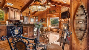 A rustic wooden cabin interior with a dining area, kitchen, and fireplace. - The Cabin at Rock Canyon (Branson)