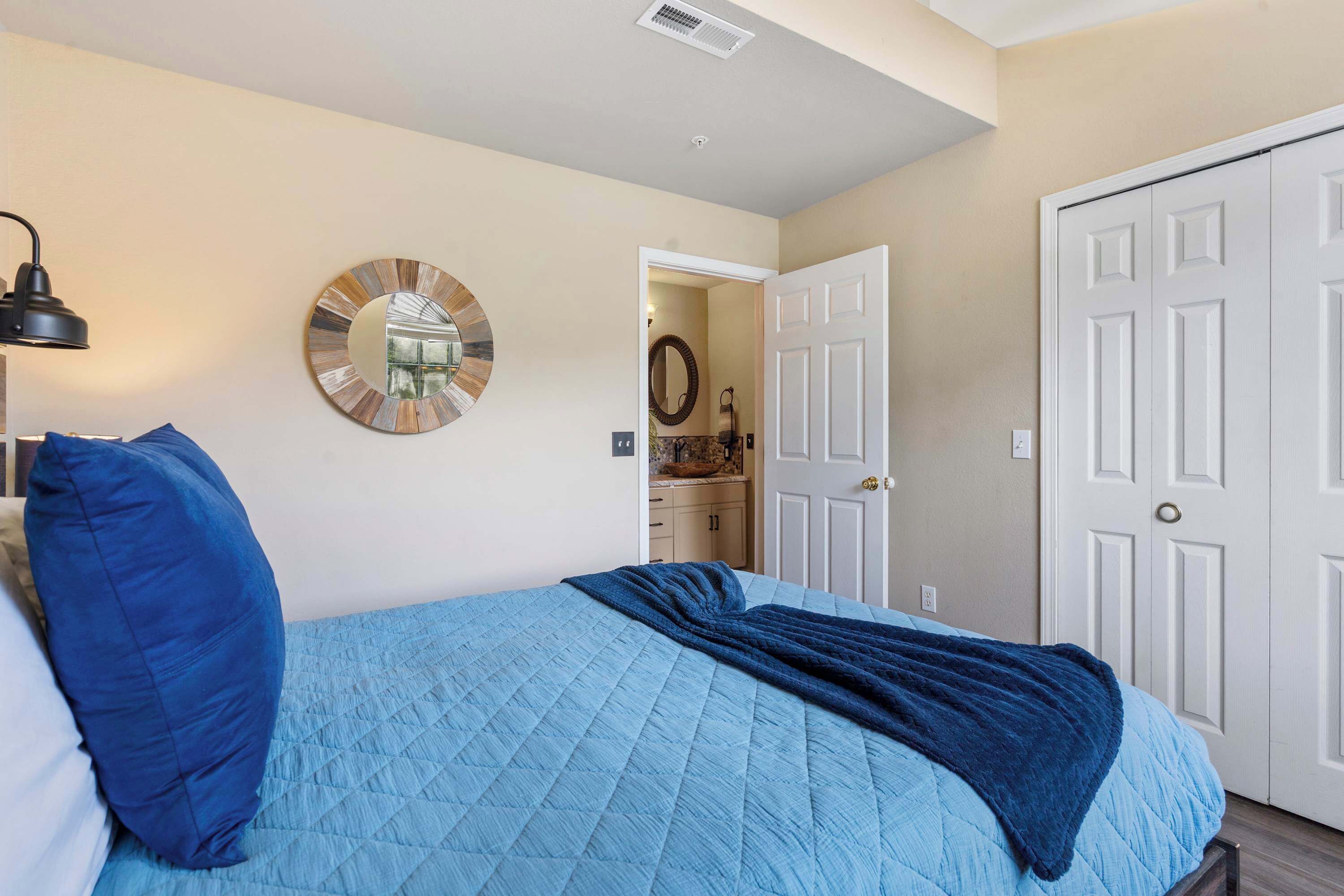 Une chambre à coucher avec un lit, un miroir rond, une porte et un luminaire fixé au mur.