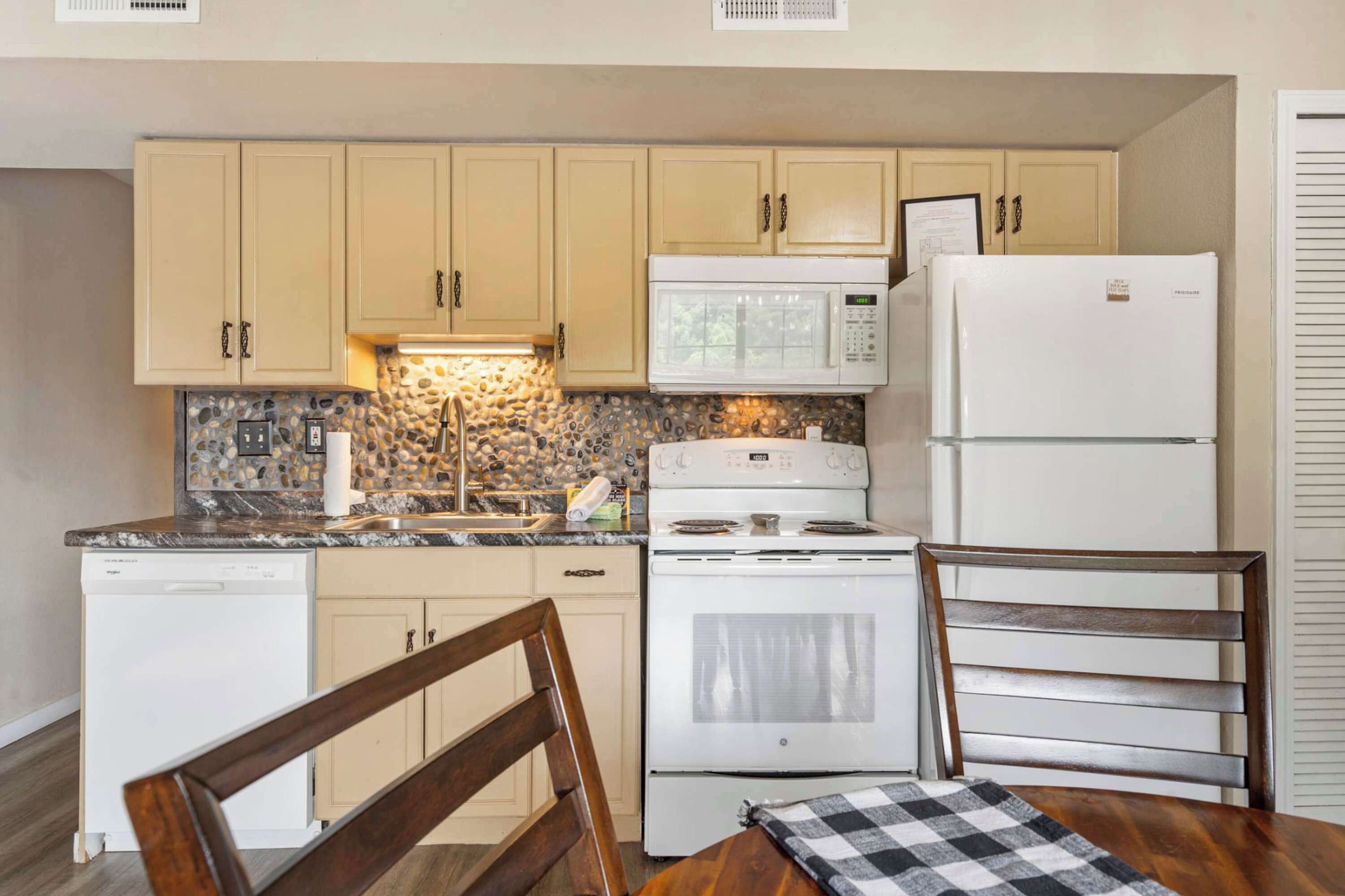 A compact kitchen with beige cabinets, a white microwave, a white refrigerator, a stove, and a dishwasher.