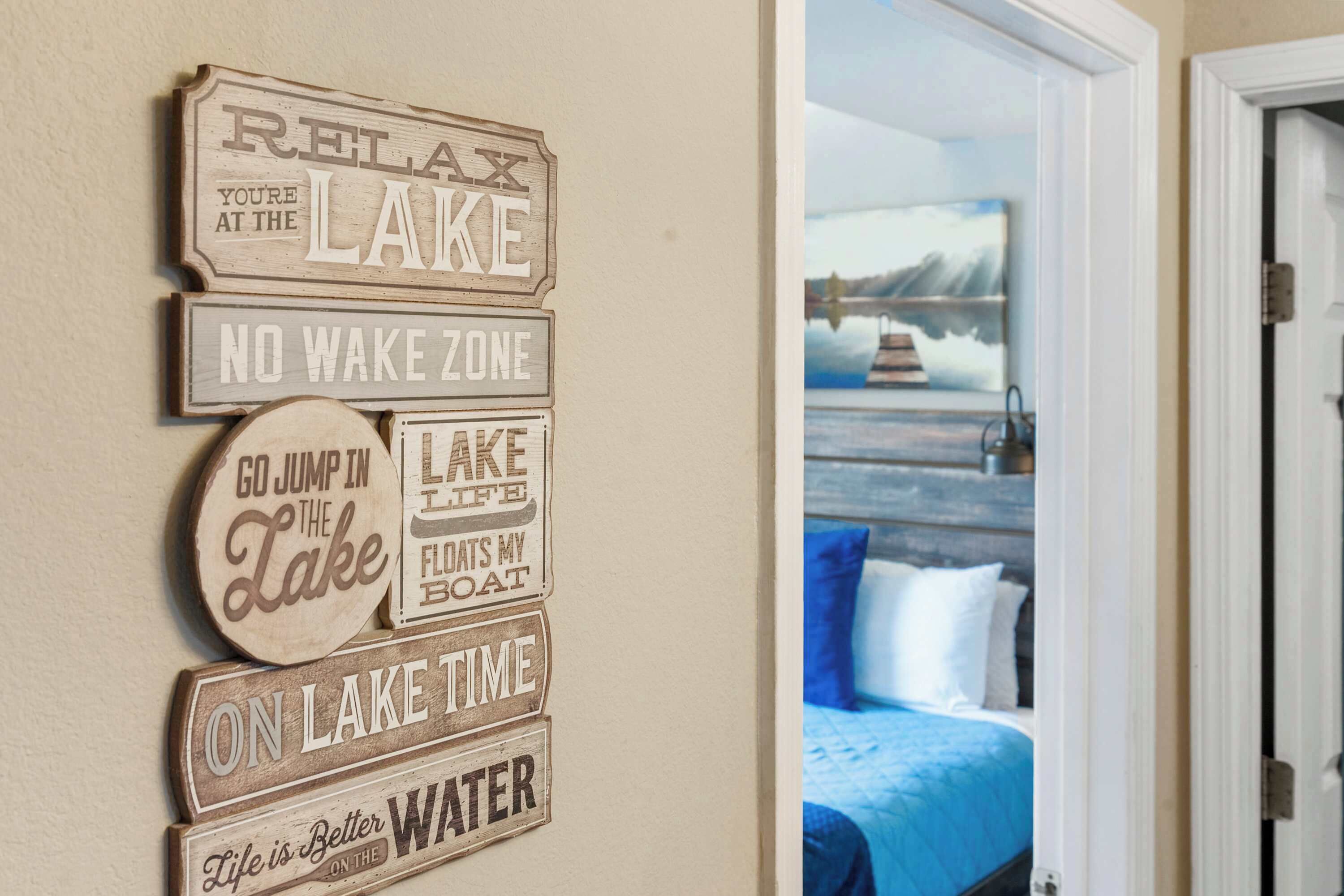 Pared decorada con letreros motivacionales con temática de lago y una vista parcial de un dormitorio con cama y un cuadro.