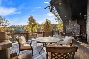 A deck with outdoor seating, a stone fireplace, and a view of trees. - The Lodge at Rock Canyon (Branson)