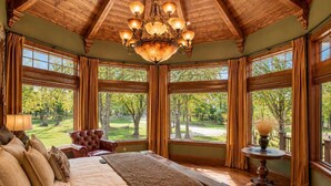 A bedroom with a large bed, a chandelier, multiple windows, and a view of a park. - The Lodge at Rock Canyon (Branson)