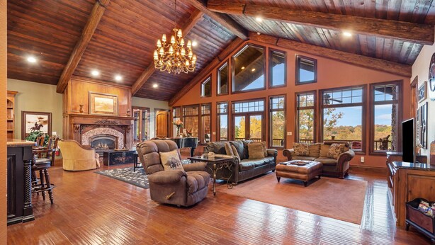 A spacious living room with a fireplace, large windows, and wooden flooring. - The Lodge at Rock Canyon (Branson)