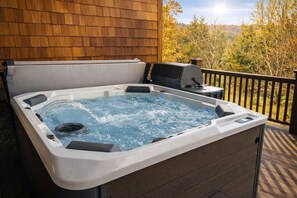 Een hottub op een houten terras met uitzicht op bomen en heuvels.