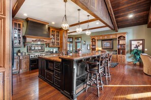 A spacious kitchen with a large island, wooden cabinets, and a high ceiling with exposed beams.