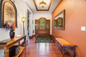 A hallway with a wooden bench, a desk with a vase of flowers, and a door with glass panels.