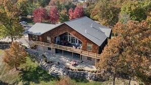 Un grand bâtiment en briques doté d’une terrasse en pierre et d’un espace extérieur aménagé pour s’asseoir, le tout entouré d’un feuillage automnal.