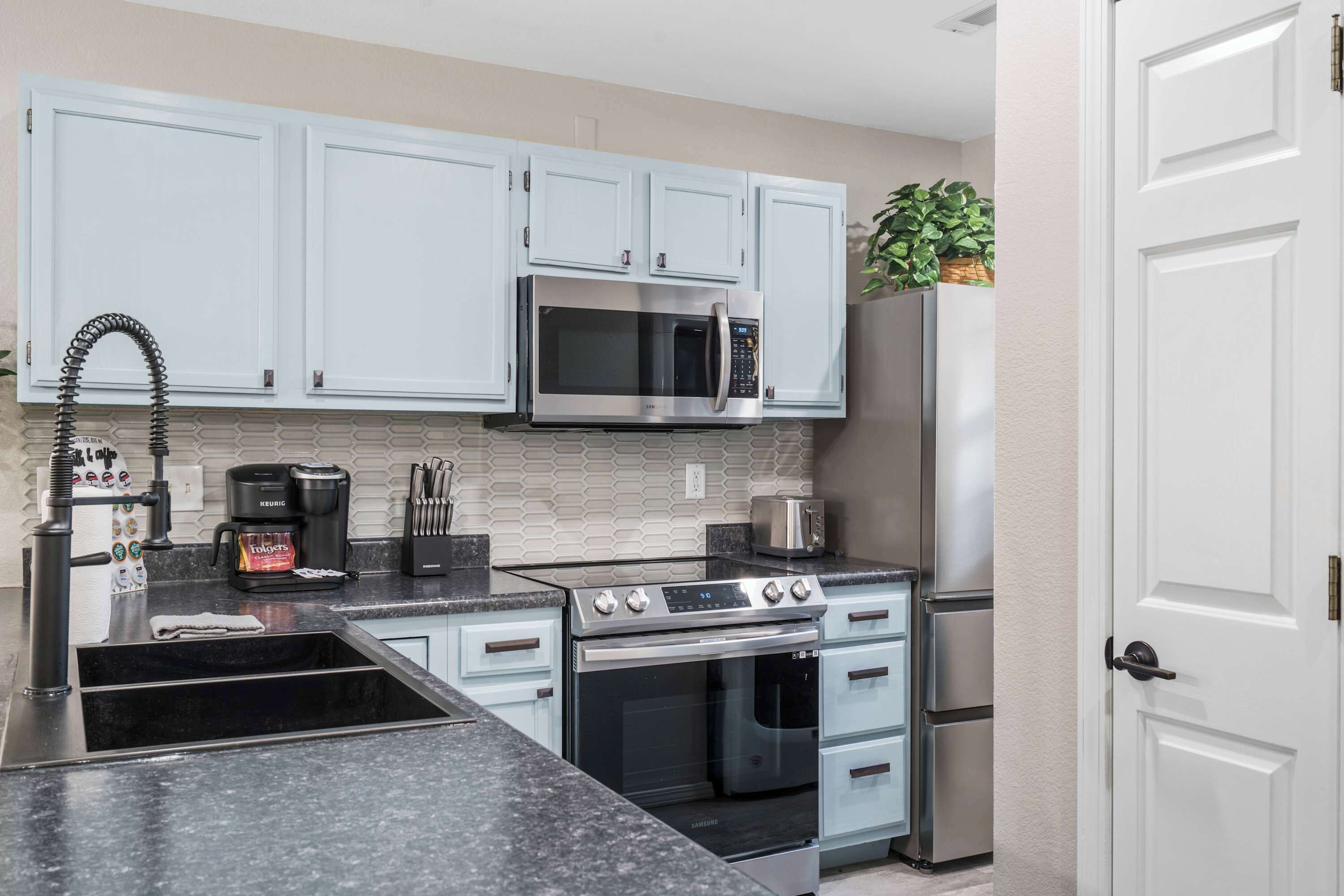 A modern kitchen with light blue cabinets, stainless steel appliances, and a black granite countertop.