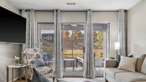 A modern living room with a sofa, armchair, and a flat-screen TV mounted on the wall. - Water's Edge & Golf Course View (Branson)