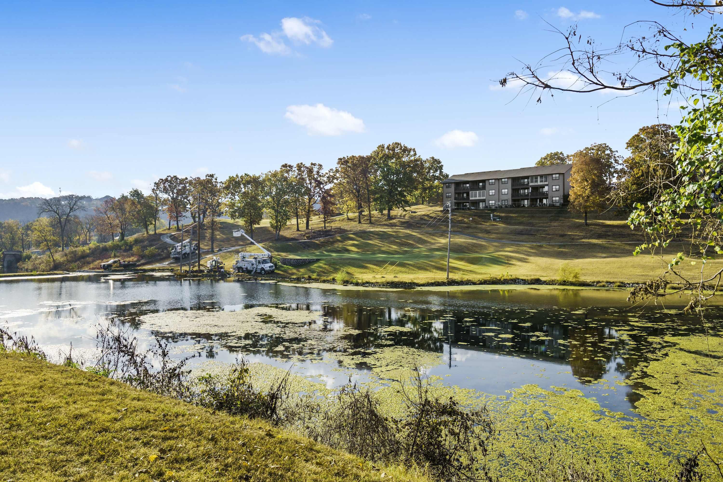 A serene landscape with a pond, trees, and a building in the background.