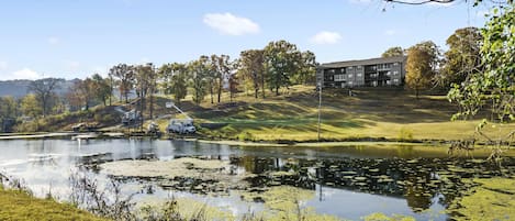 A serene landscape with a pond, trees, and a building in the background.