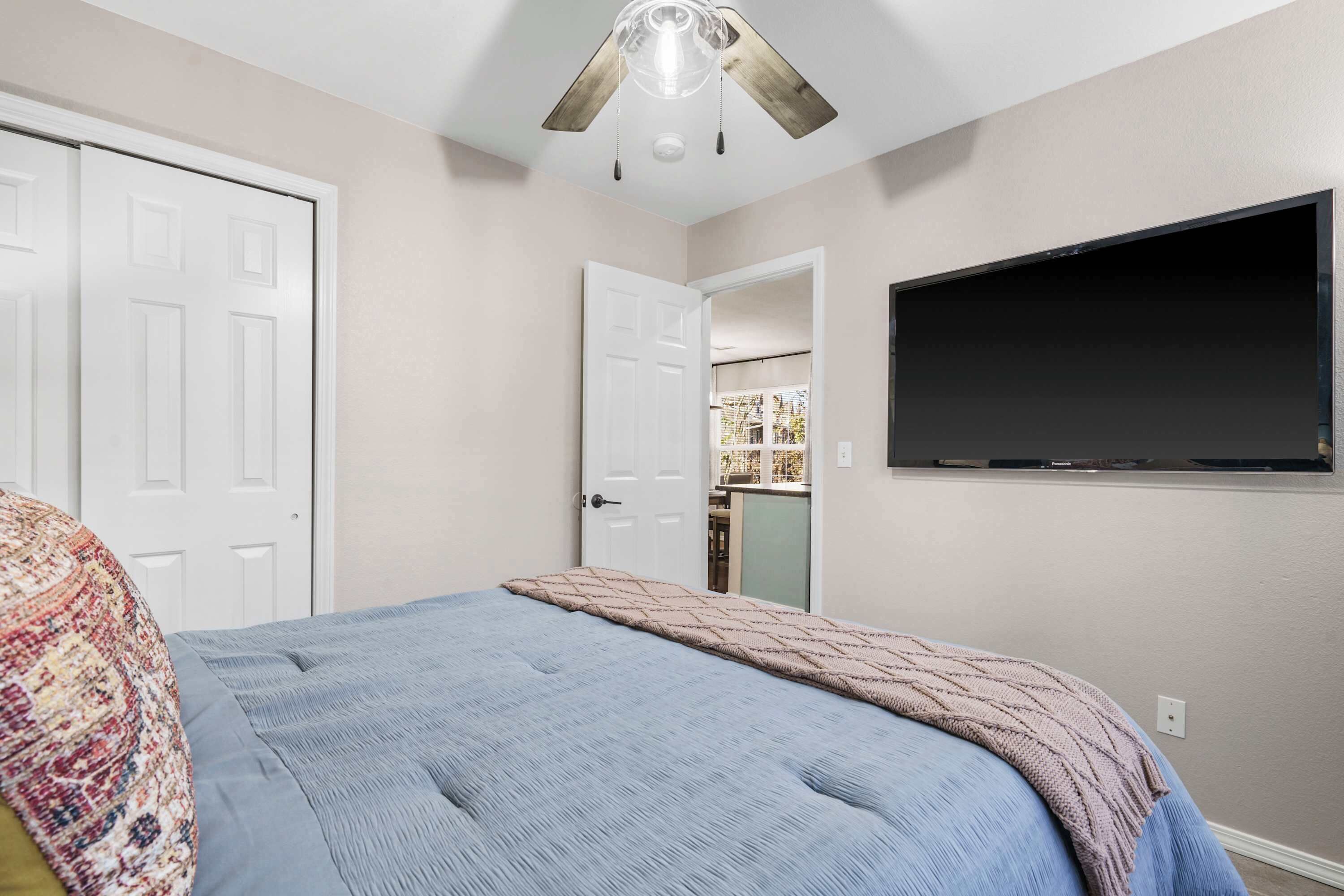 A bedroom with a bed, a ceiling fan, and a TV on the wall.