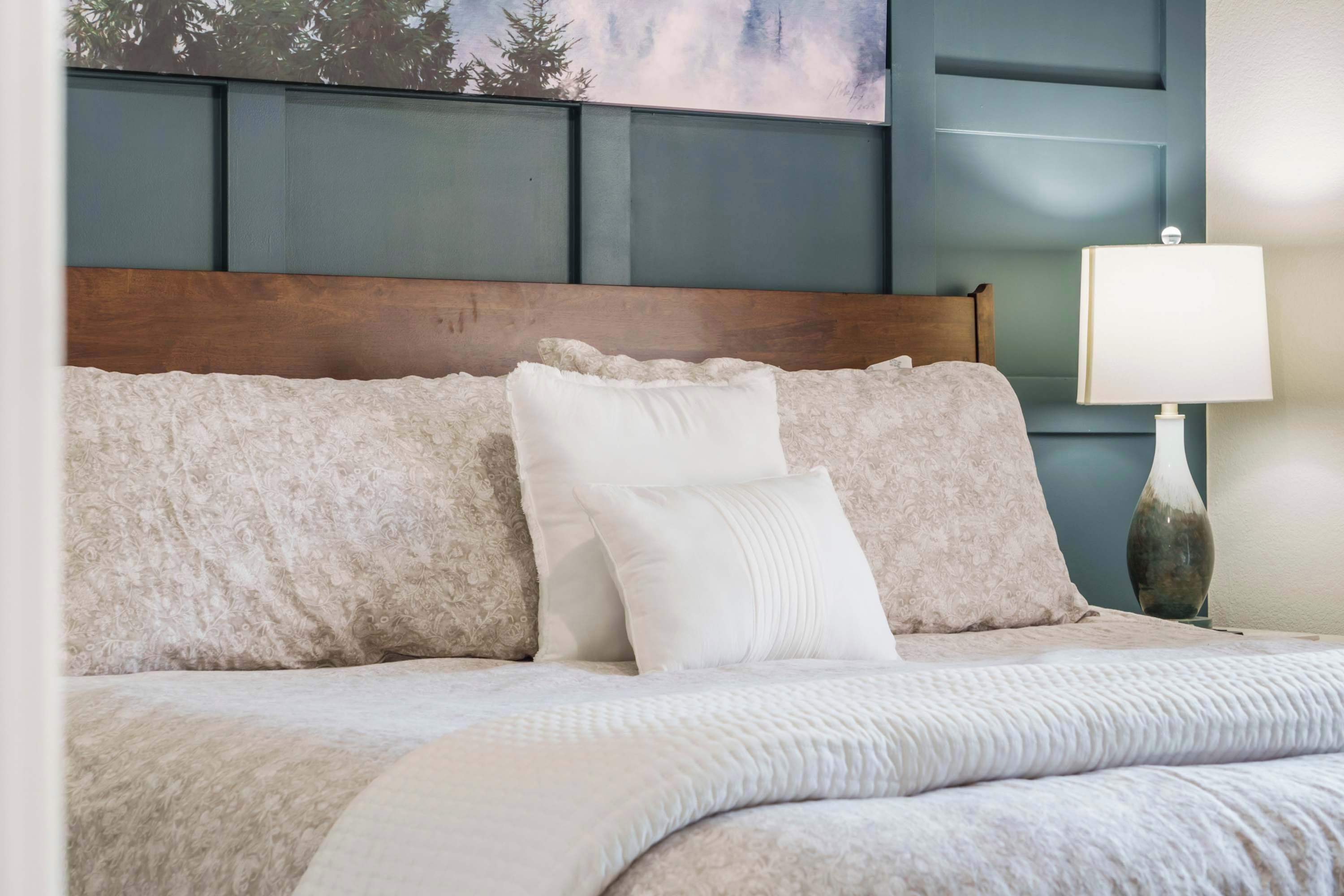Un lit bien fait, avec une tête de lit en bois, une lampe blanche et un tableau accroché au mur.