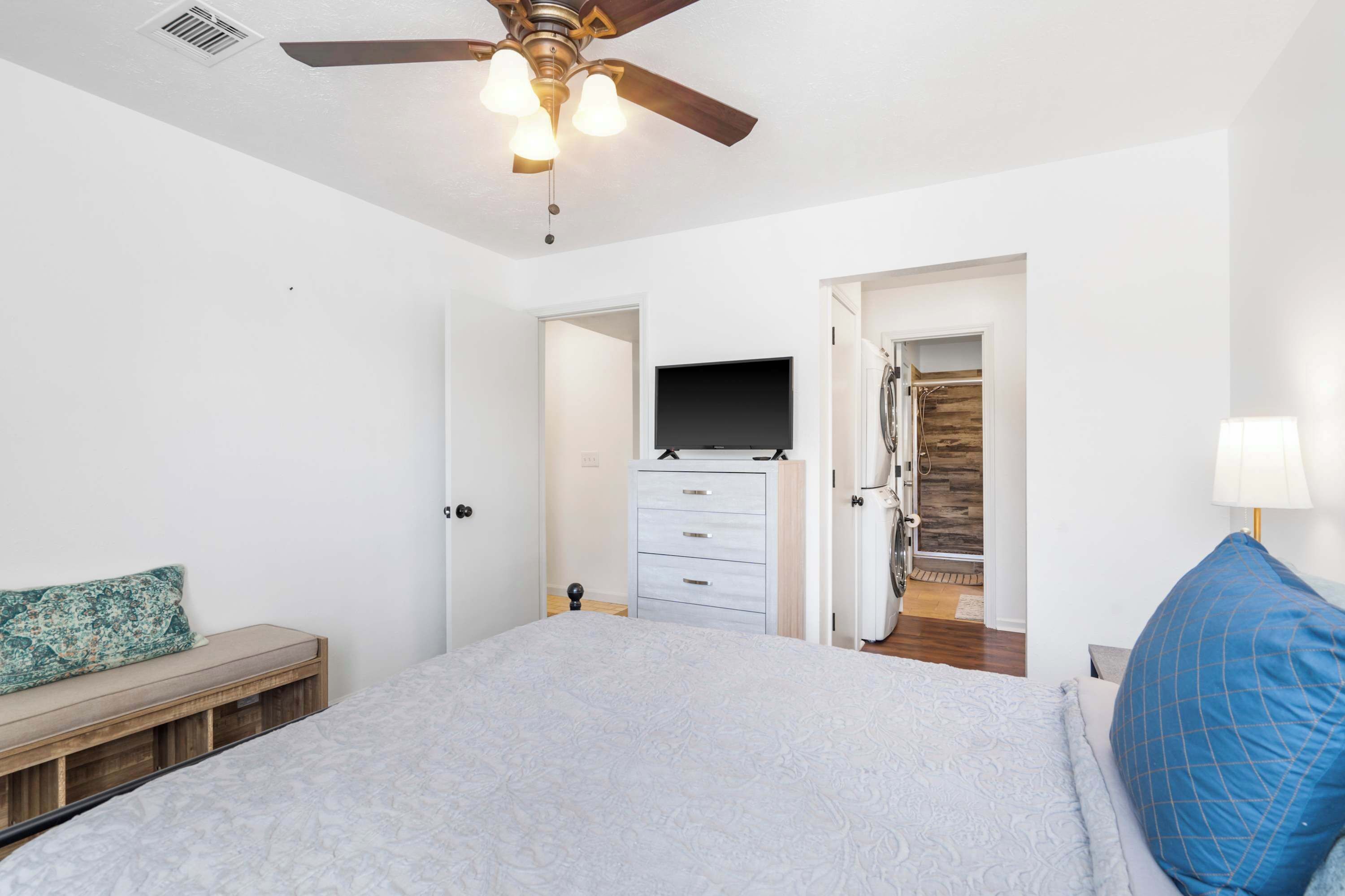 Habitación con cama, ventilador de techo, televisor, armario y baño visible a través de una puerta abierta.