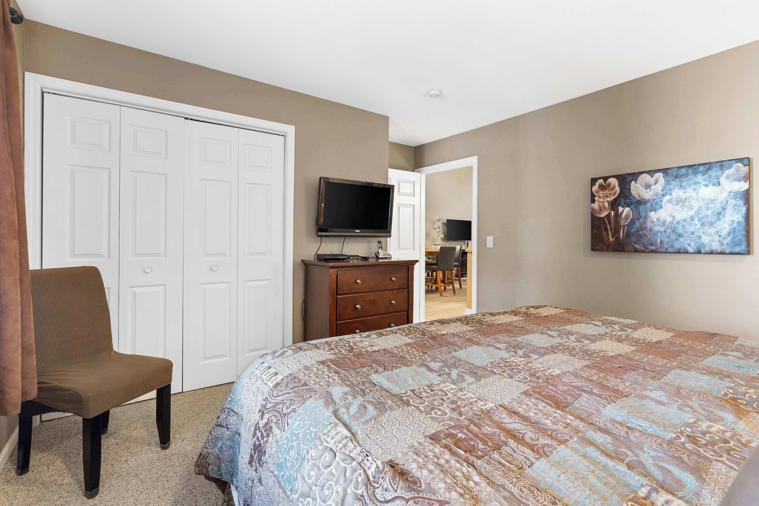A bedroom with a large bed, a TV, a dresser, and a chair.