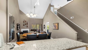 A modern kitchen with a granite countertop, dining area with chairs, and a staircase.