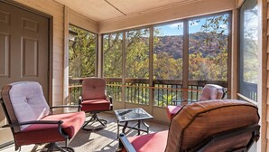 A balcony with two chairs and a small table, overlooking a scenic view of trees and hills. - Whispering Water @ Pointe Royale (Branson)