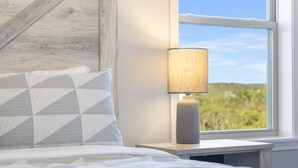 A bedroom with a bed, a nightstand, a lamp, and a window with a view of greenery. - Stonebridge Escape Sleeps 8! (Branson West)