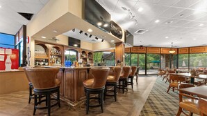 A bar area with a sign reading 'LEDSHIRE GRILL,' bar stools, a counter with various bottles, and a view of greenery outside. - Stonebridge Escape Sleeps 8! (Branson West)