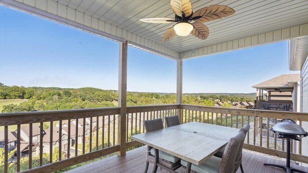 A covered outdoor deck with a table and chairs, a ceiling fan, and a view of a green landscape. - Stonebridge Escape Sleeps 8! (Branson West)