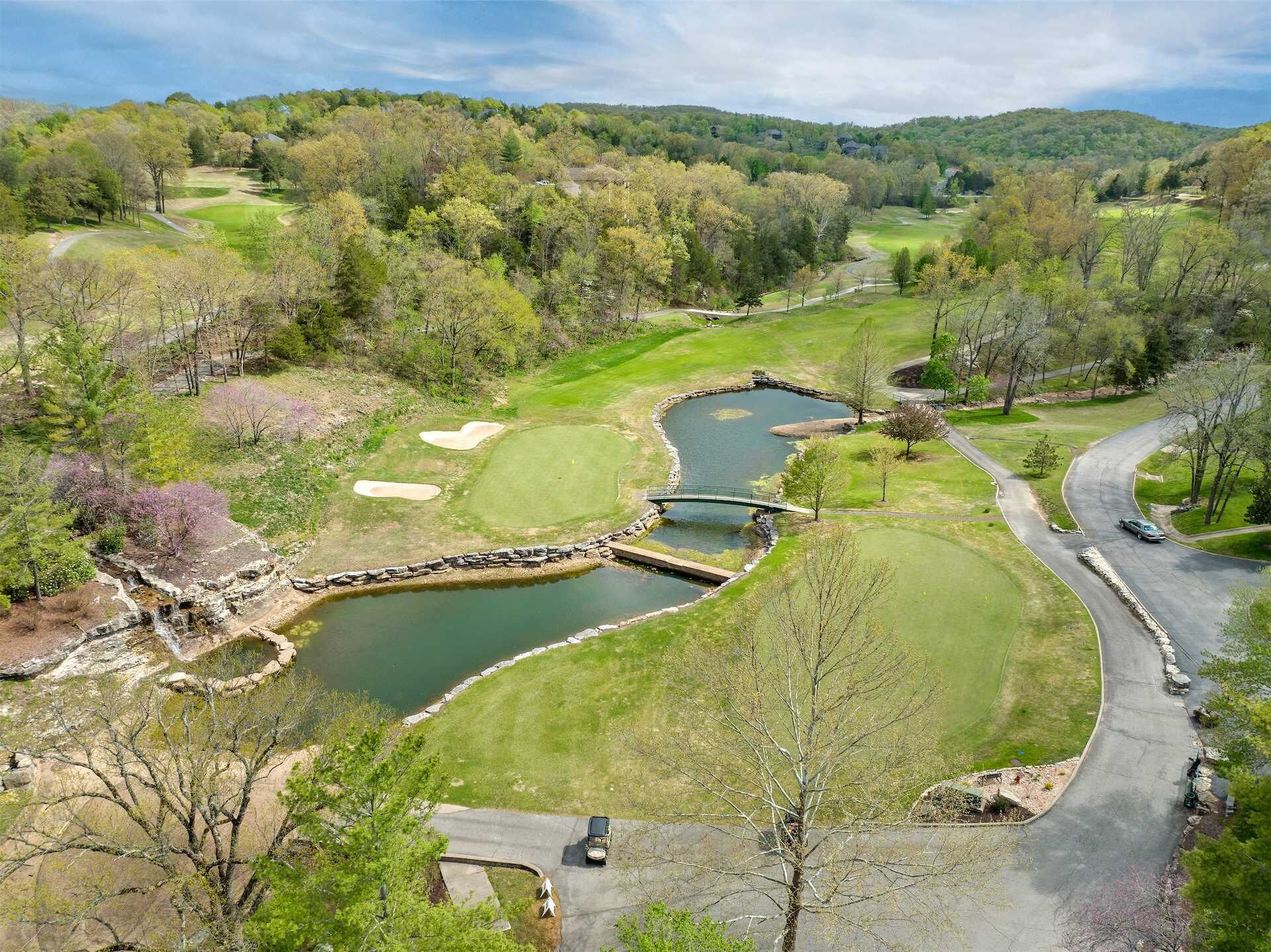 A golf course with a pond, a bridge, and a winding road.
