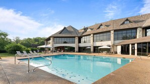 A pool area with lounge chairs, a stone deck, and a large building with multiple windows and a stone facade. - Stonebridge Escape Sleeps 8! (Branson West)