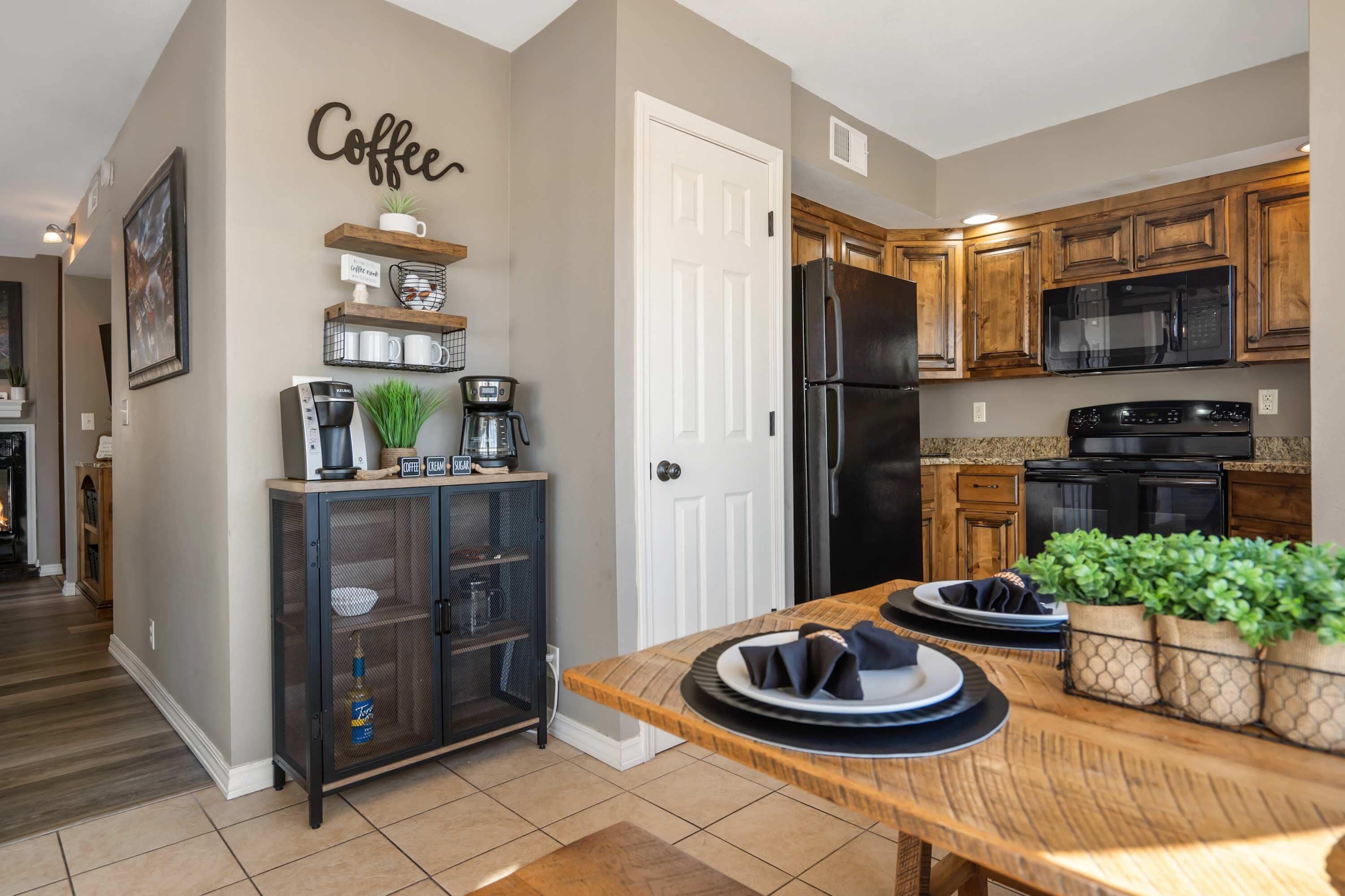 A kitchen with wooden cabinets, a black refrigerator, a microwave, and a coffee station.