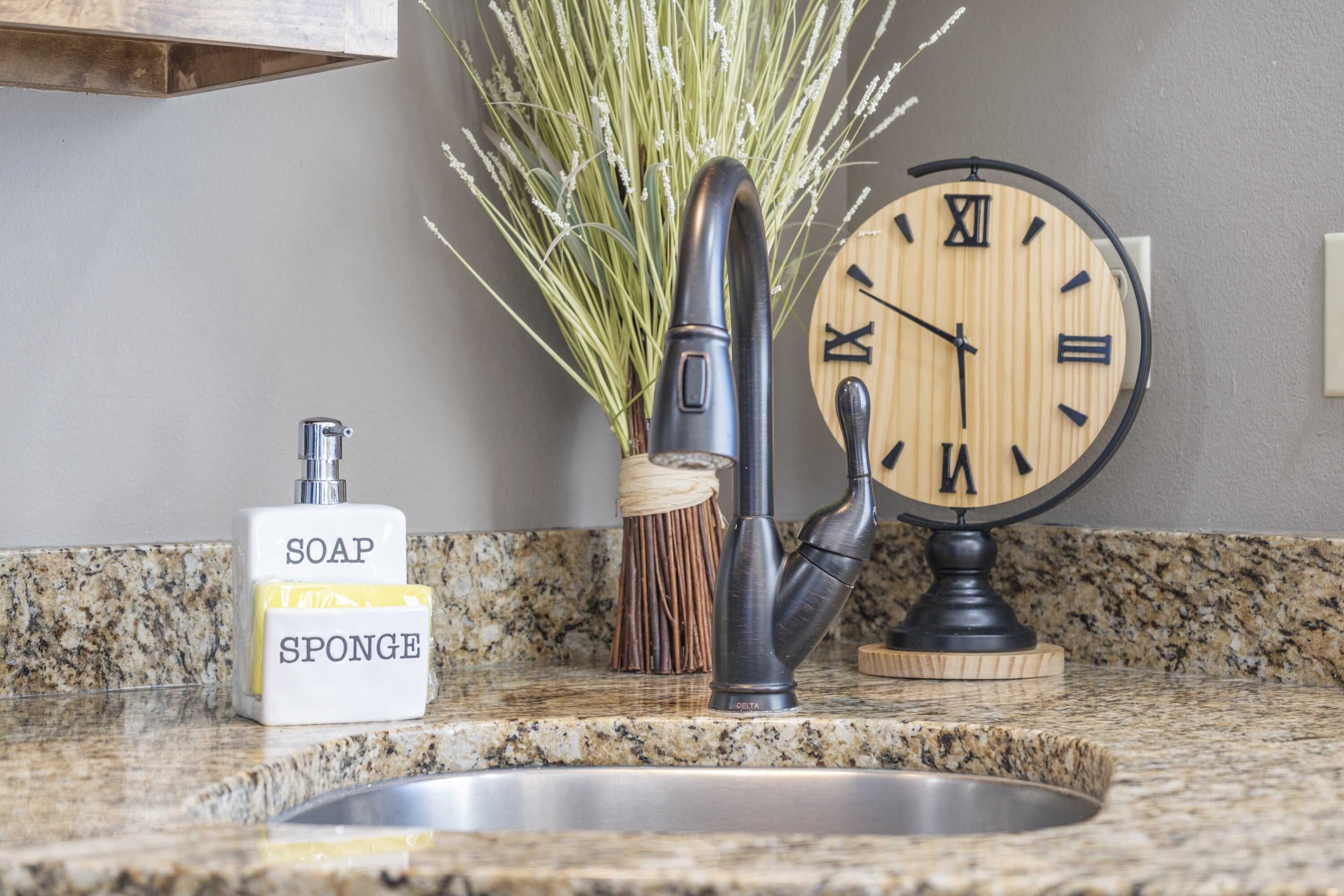 A kitchen sink with a faucet, a soap dispenser, and a wall-mounted clock.