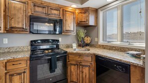 A kitchen with wooden cabinets, a black stove, a microwave, and a dishwasher. - Lakescape at The Getaways (Kimberling City)