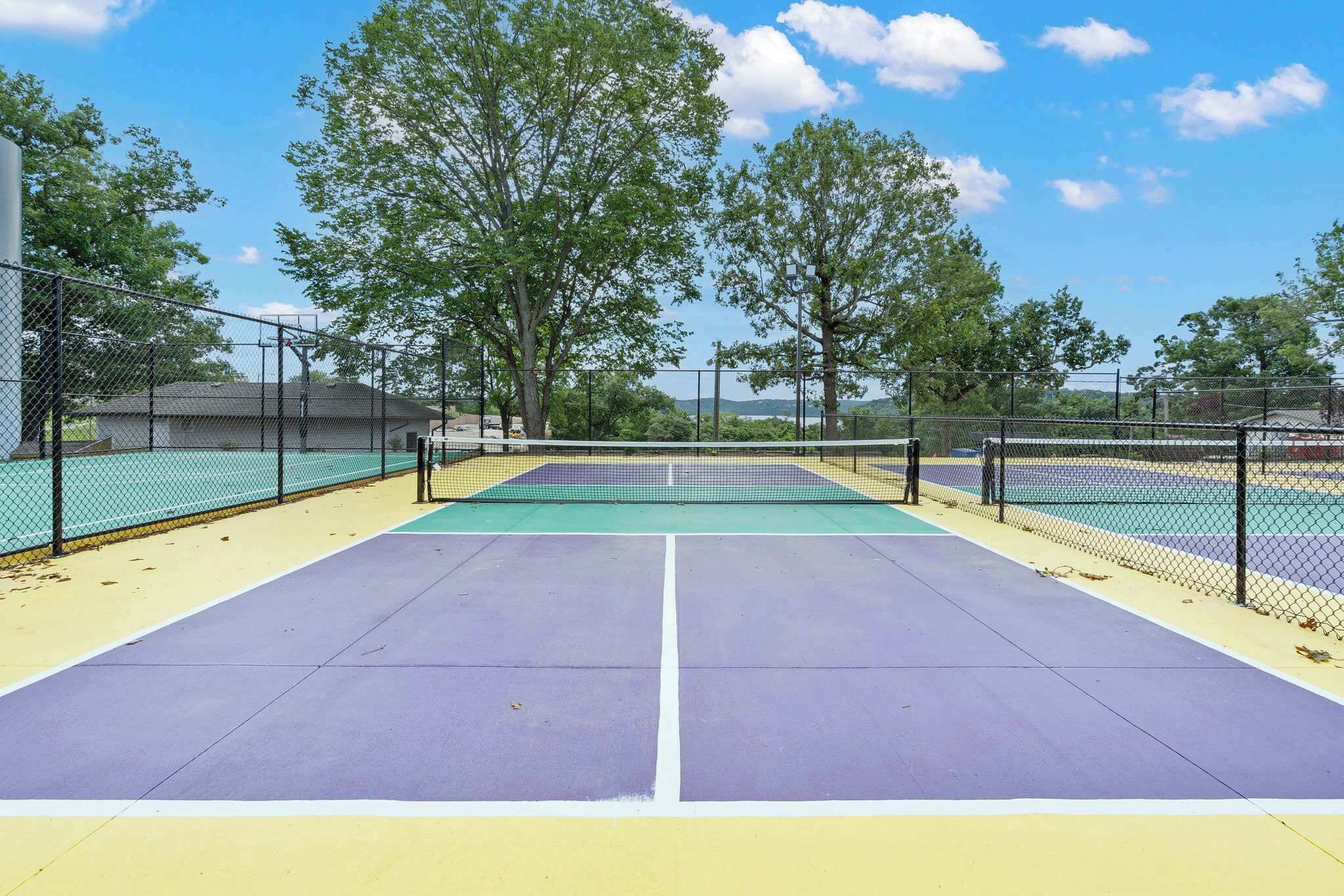 Een tennisbaan met een net, omgeven door bomen en een hek.