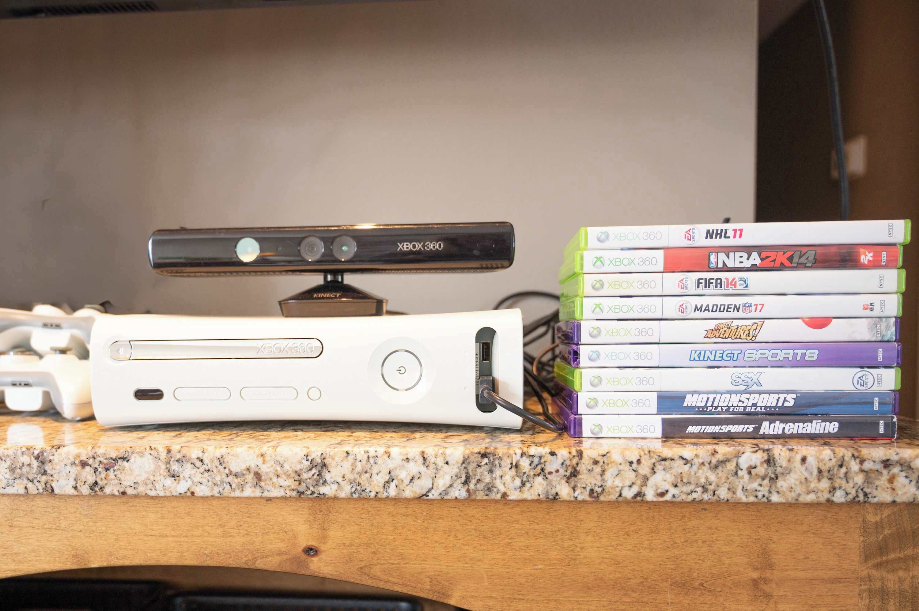 A gaming console and a stack of Xbox 360 video game cases on a countertop.