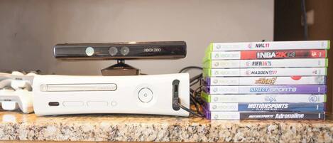 A gaming console and a stack of Xbox 360 video game cases on a countertop.